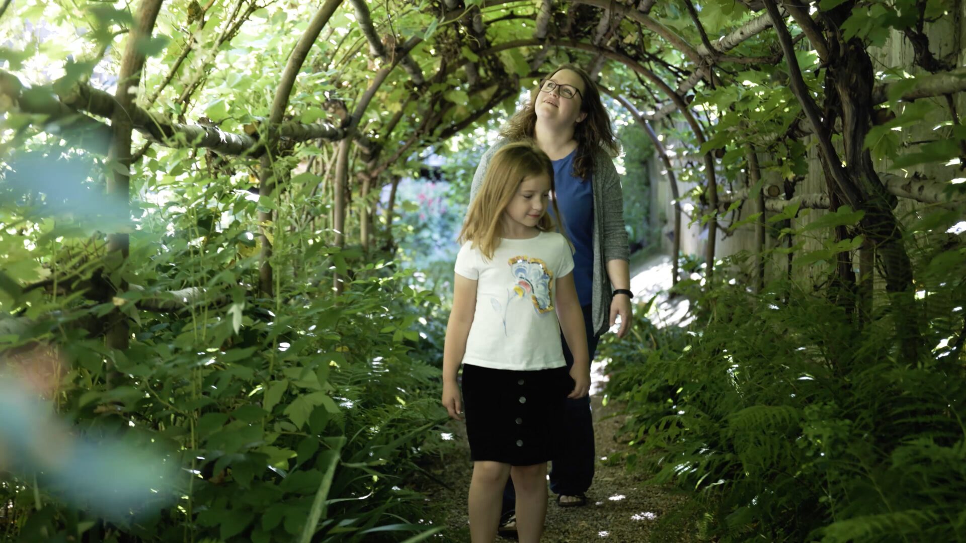 A parent with her child walking through a long green tunnel in the garden of The Great Hall