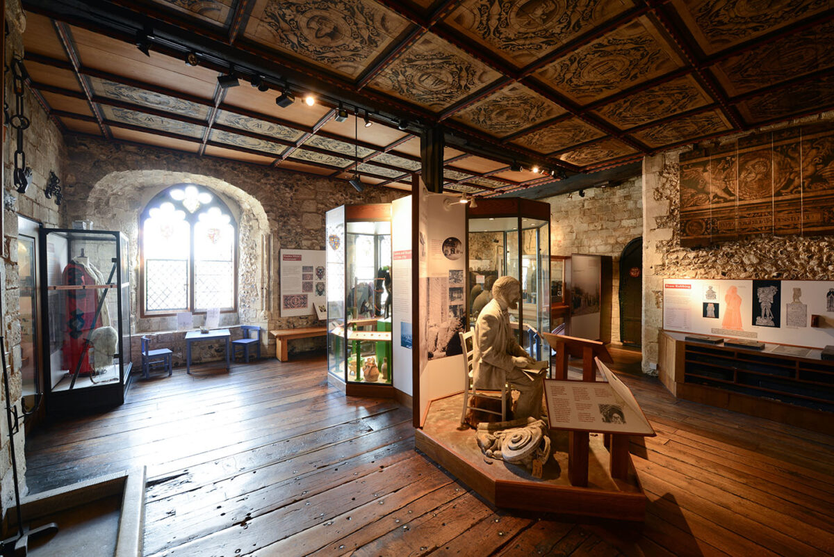 The interior of a museum, the floors and ceiling are covered in wood and there are glass displays of old artifacts