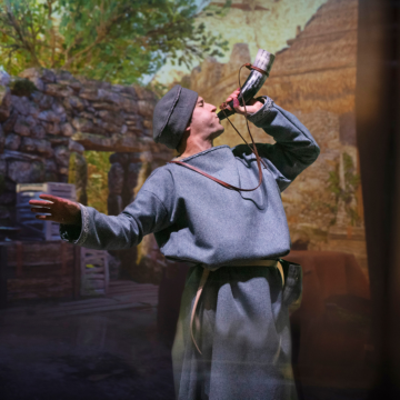 A man in Anglo Saxon attire blows a horn into the sky