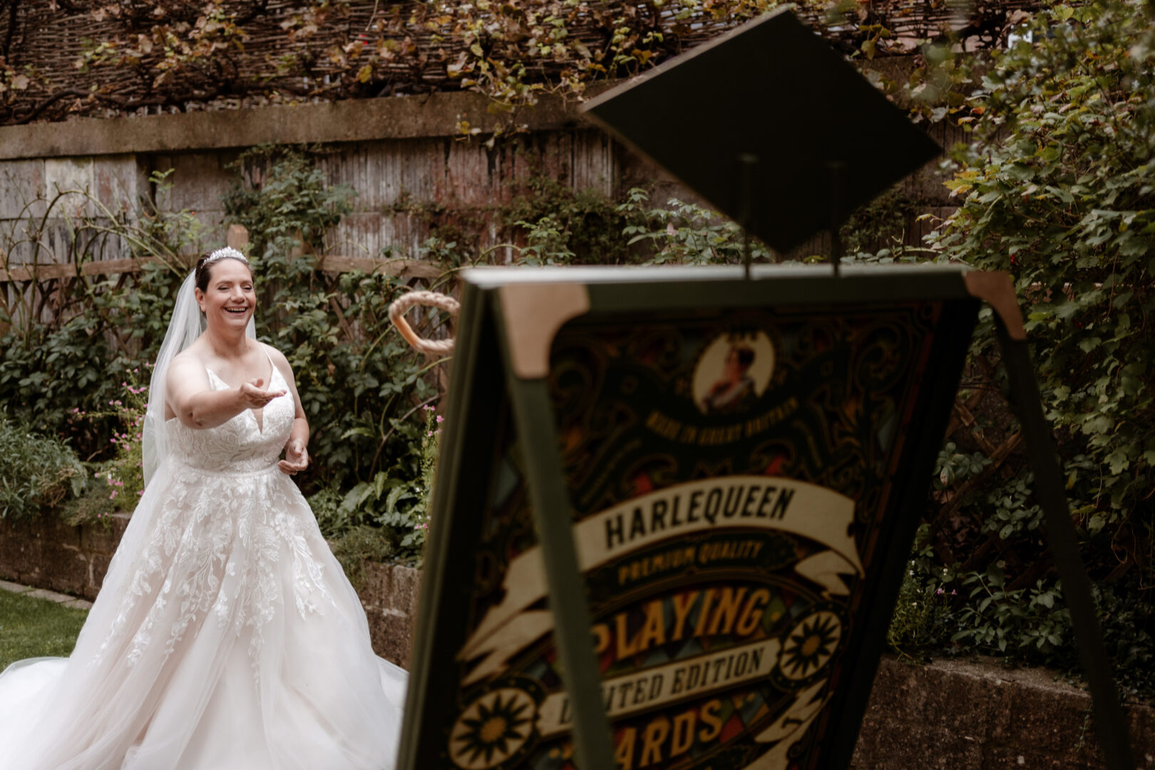 A lady in a long white wedding dress plays a hoop game in a garden