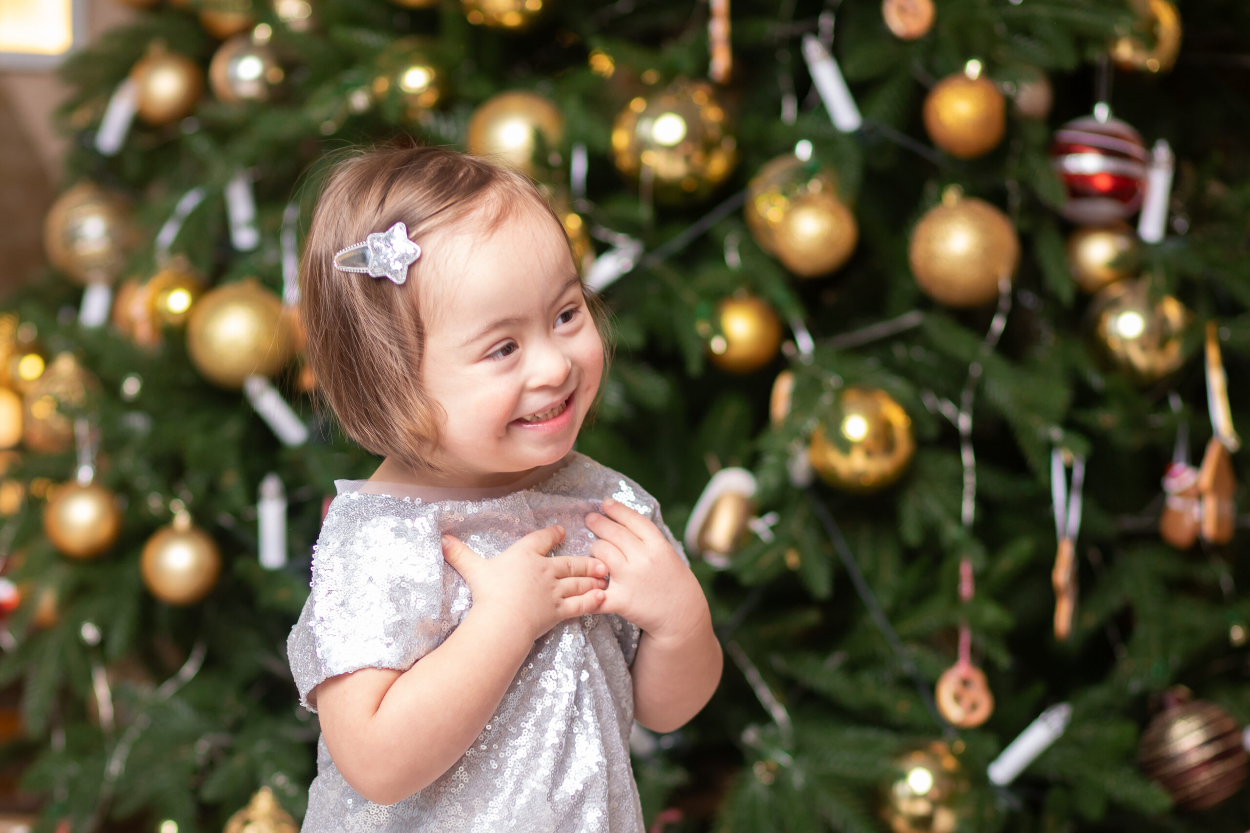 A young girl with Down Syndrome excited in front of a Christmas tree