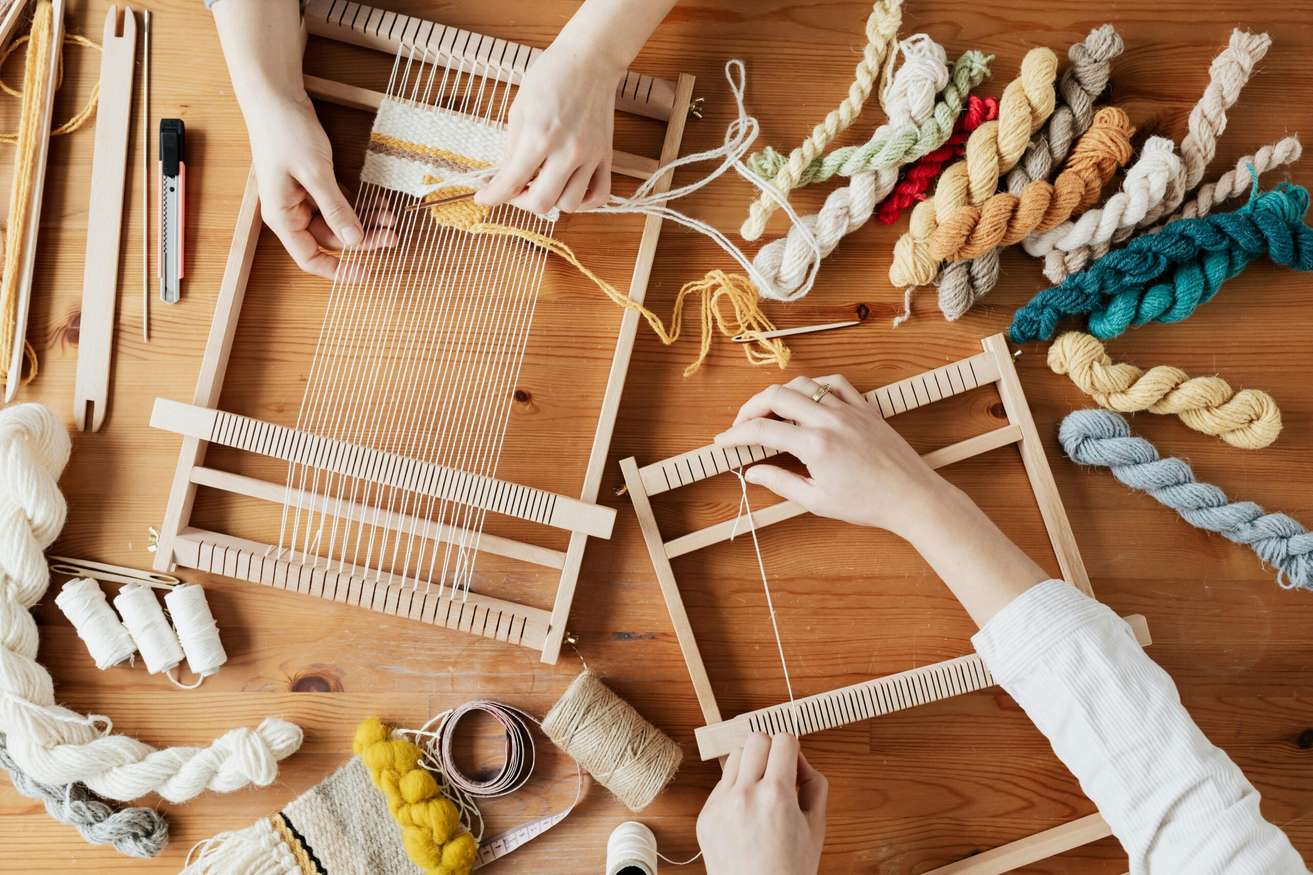 Two hands weaving using small wooden looms