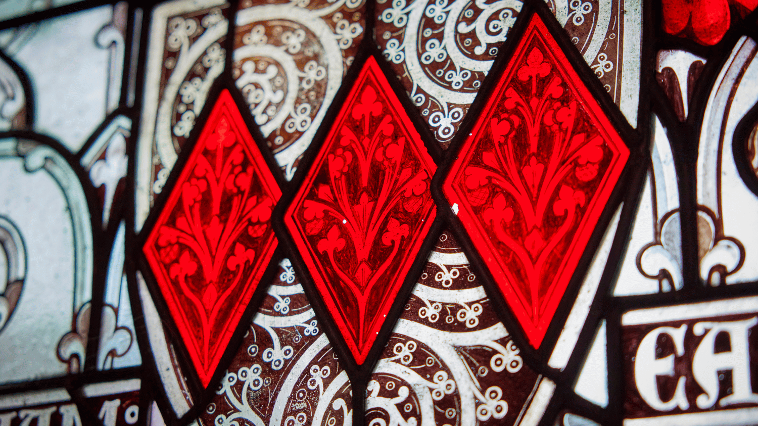 A stained glass window up close depicting vibrant red diamonds with flowers inside.
